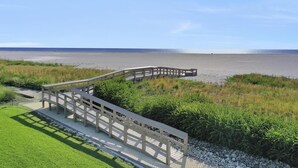 Een houten bruggetje naar een strand onder een heldere lucht.
