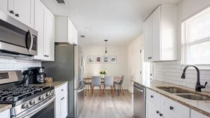 A modern kitchen with white cabinets, stainless steel appliances, and a central island with chairs. - Spacious 4BR Home, Central Georgetown Location! (Georgetown)