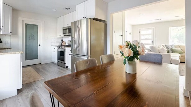 A modern kitchen with white cabinets, stainless steel appliances, and a dining area with a wooden table and chairs. - Spacious 4BR Home, Central Georgetown Location! (Georgetown)