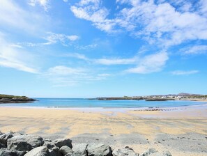 A beach with a clear sky, rocky foreground, and distant buildings. - Beach Court Hideaway (Holyhead)