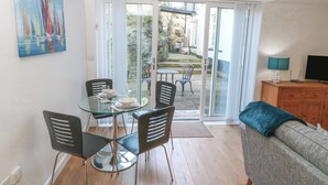 A room with a glass table and chairs, a sofa, a TV, and a painting on the wall. - Beach Court Hideaway (Holyhead)