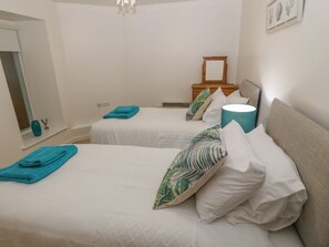 Une chambre avec deux lits, chacun agrémenté d’une serviette turquoise et d’un oreiller blanc orné d’un motif de feuilles. Une lampe de chevet se trouve sur l’un des lits et une tête de lit en bois sur l’autre.