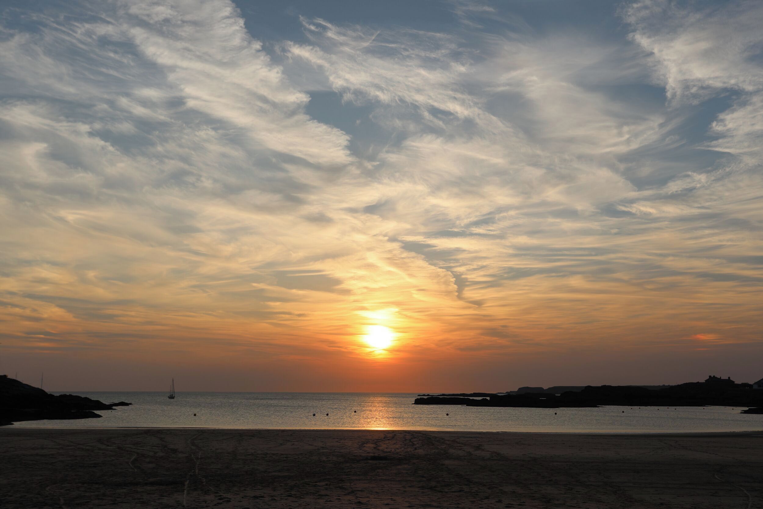 Une plage au coucher du soleil, avec une mer calme et des formations rocheuses lointaines.