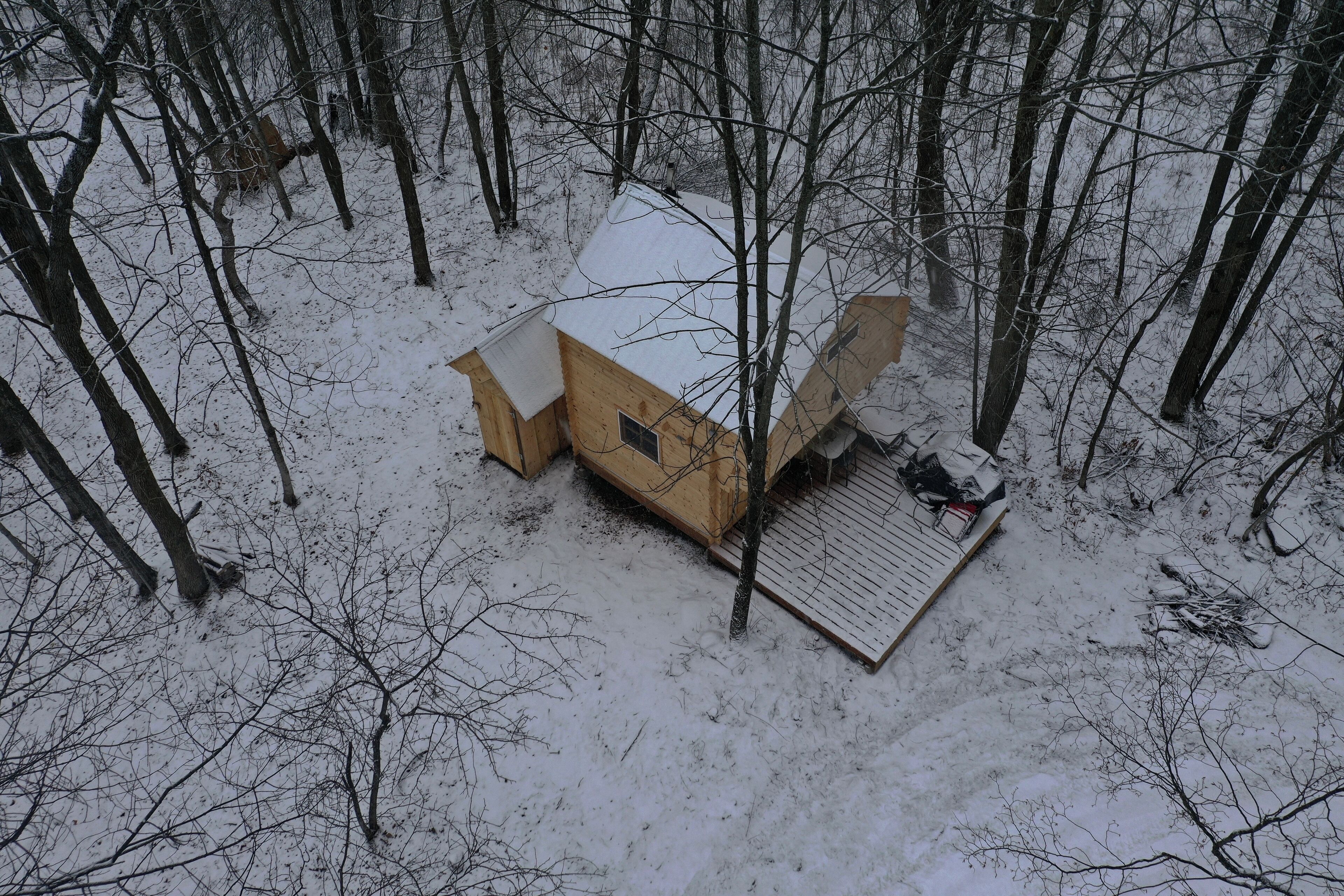 A wooden cabin with a sloped roof and a small porch area, surrounded by a snowy forest.