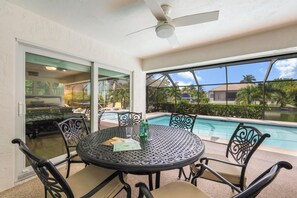 A covered outdoor area with a pool, a table with chairs, and a ceiling fan. - Waterfront Home With Table Tennis, Pool and Dock (Marco Island)
