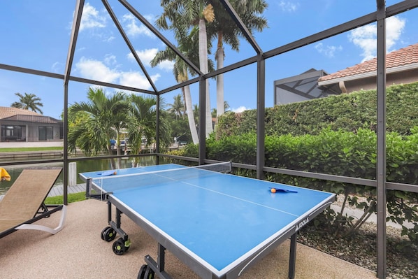 A ping pong table in an outdoor area with a view of palm trees and a building in the background. - Waterfront Home With Table Tennis, Pool and Dock (Marco Island)