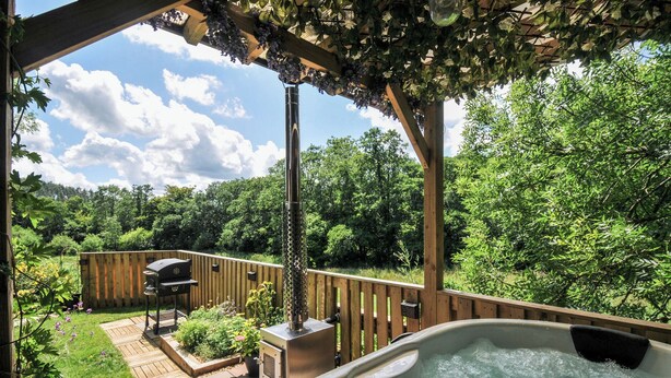 Ein Whirlpool unter einer Pergola mit einer Holzterrasse und einem Grill.