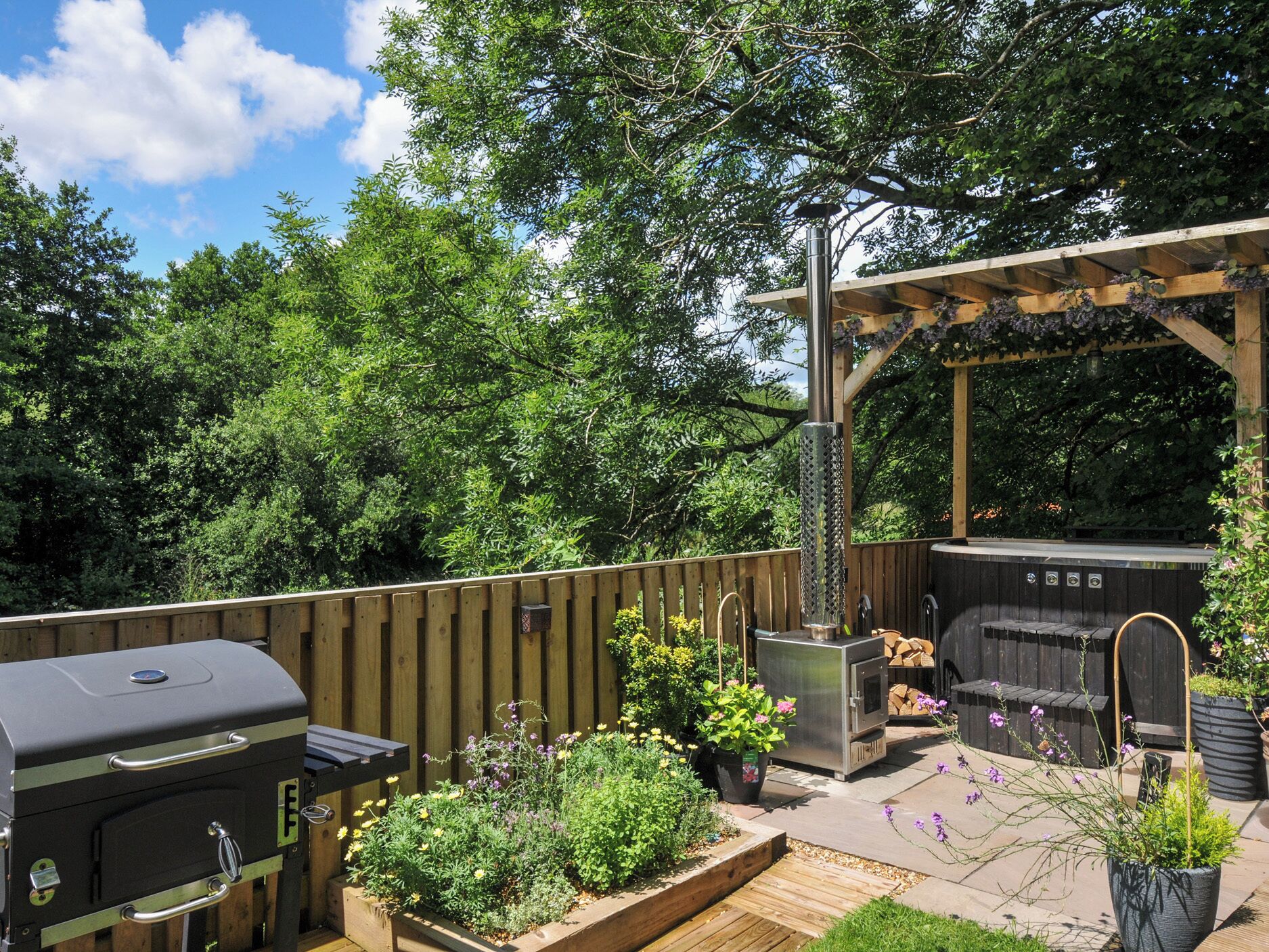 An outdoor patio with a barbecue grill, a wood-fired oven, and a pergola with hanging plants.