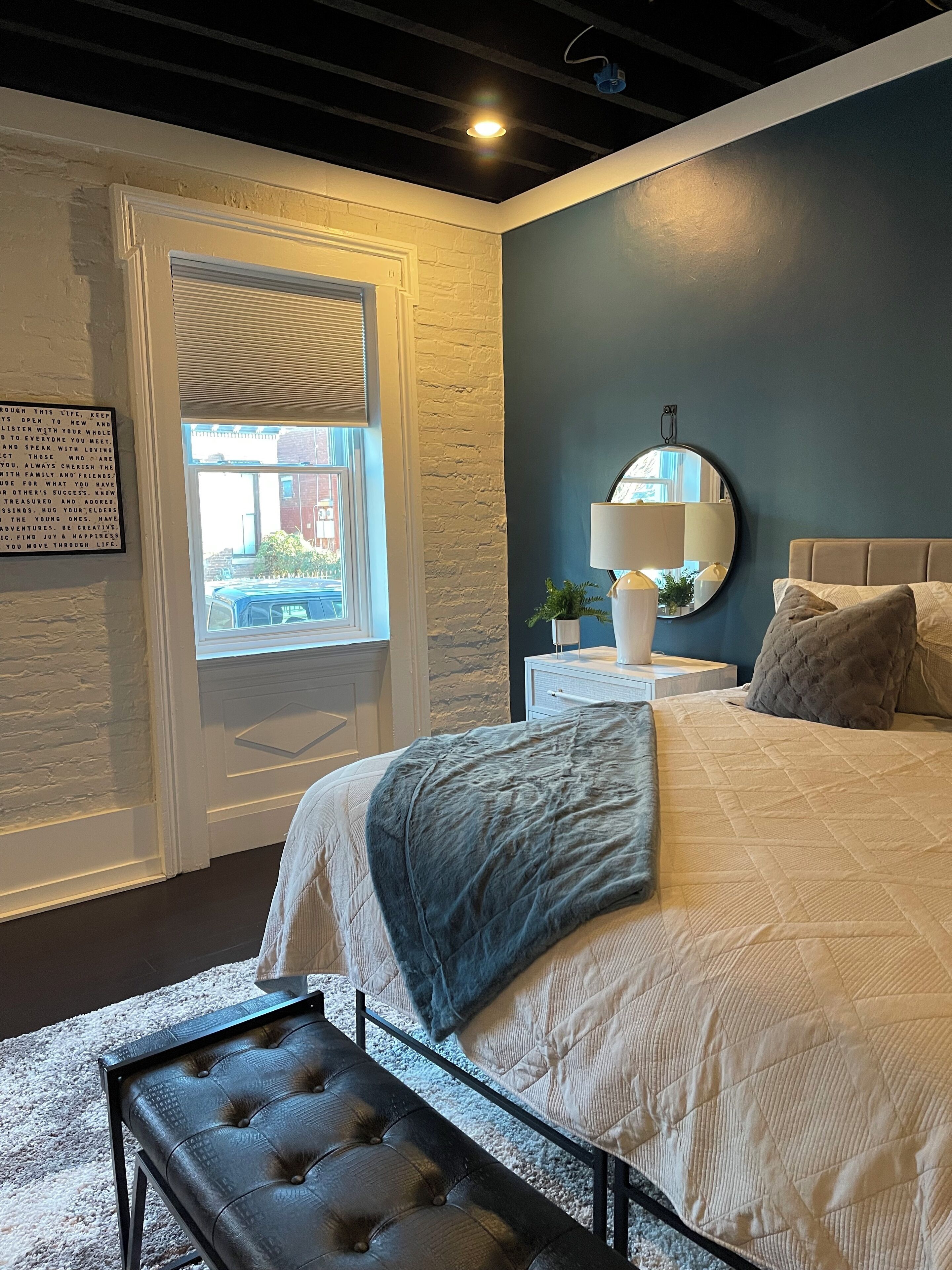 Une chambre à coucher avec un lit, une table de chevet, une lampe et une fenêtre donnant sur l’extérieur.