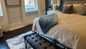 Un dormitorio con cama, mesita de noche, lámpara y un banco.