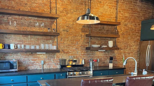 Cocina moderna con pared de ladrillo, electrodomésticos de acero inoxidable y taburetes de bar.