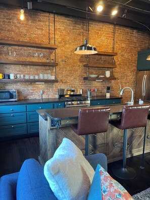 A modern kitchen with a brick wall, stainless steel appliances, and bar stools.
