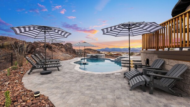 Zona de piscina con sillones de descanso y sombrillas, rodeada por una terraza de piedra y una barandilla de madera.