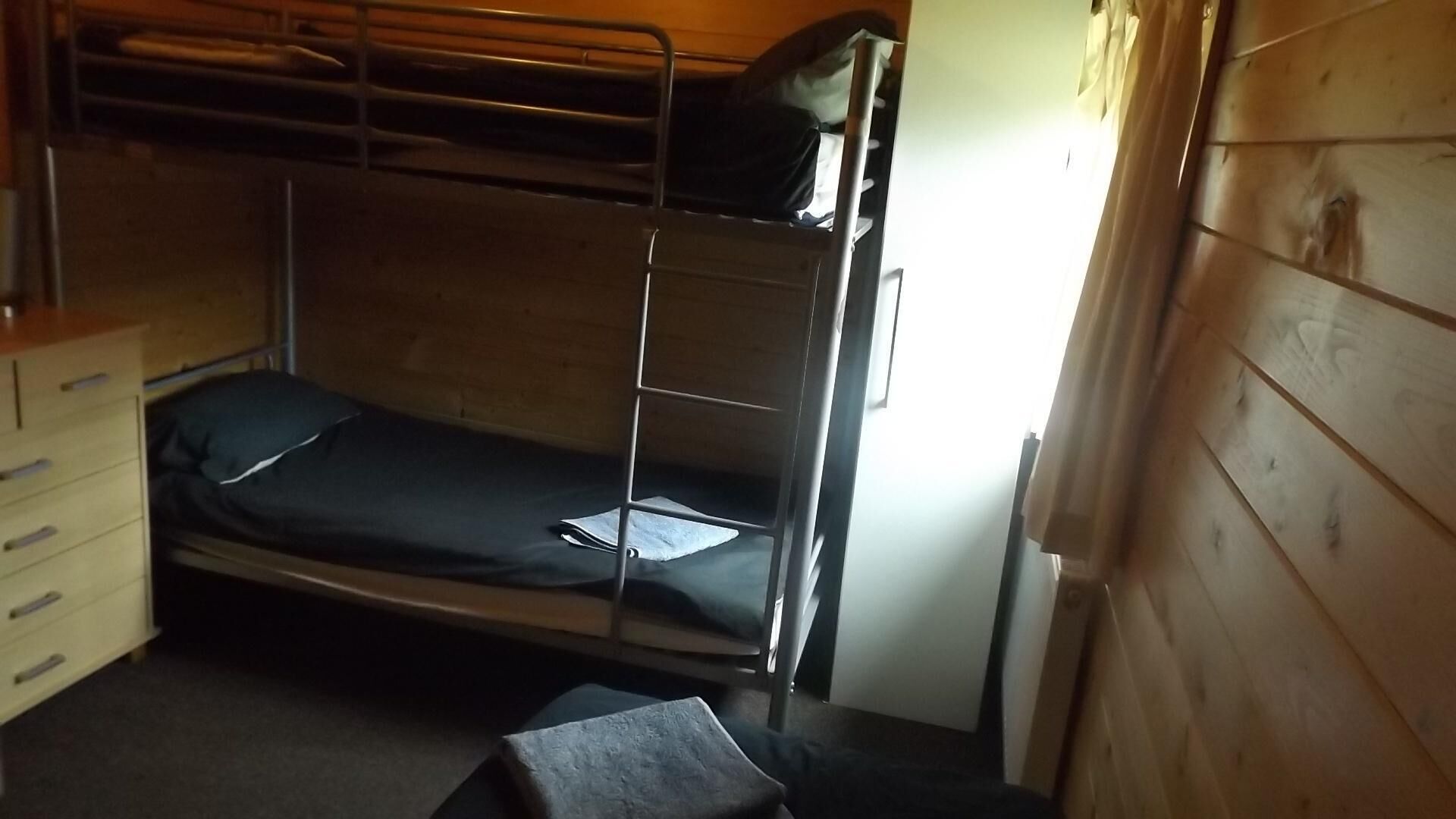 Une chambre avec un lit superposé, un mur en bois, un petit bureau et une chaise.