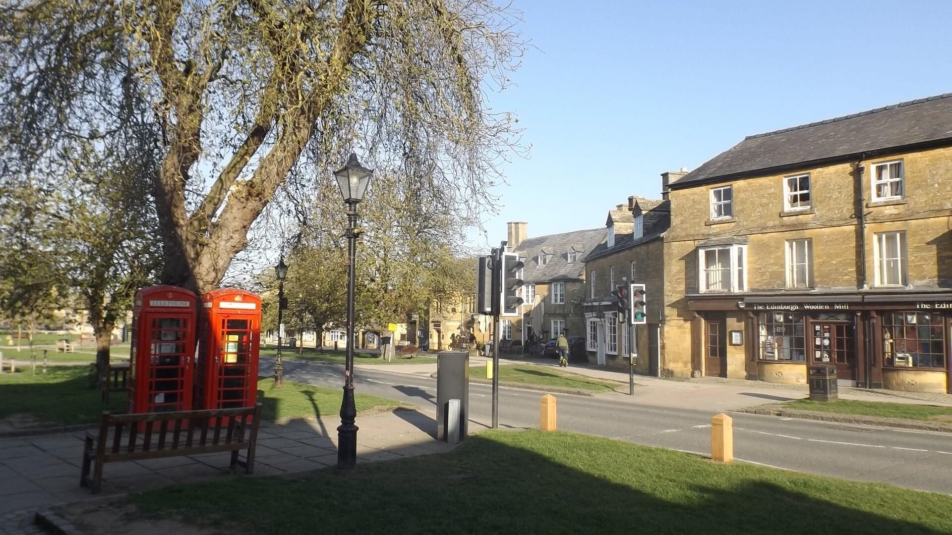 Eine Straßenszene mit einer roten Telefonzelle, einem Laternenpfahl und einem Gebäude mit der Aufschrift 'The Edinburgh Woollen Mill'.