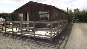 Una cabaña de madera con terraza, una parrilla de barbacoa y una mesa de picnic.