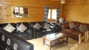 A cozy log cabin interior with a black leather sofa set, a brown leather sofa, a wooden coffee table, and a television. - Spacious 3 Bedroom Cabin at Avonvale Holiday Lodge (Evesham)