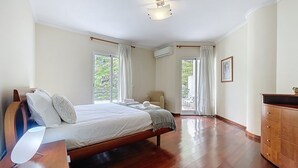 Un dormitorio con una cama de madera, una mesita de noche, un aparador y vistas al exterior a través de una puerta corrediza de vidrio.