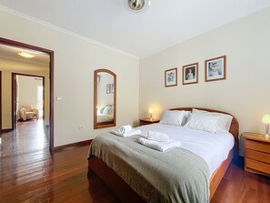 Een slaapkamer met een bed, nachtkastjes, een spiegel en ingelijste foto’s aan de muur.