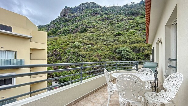 Un balcón con sillas y una mesa de metal blanco, con vistas a una exuberante colina verde.