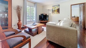 Una sala de estar con sofá, mesa de centro, televisor y un amplio ventanal.