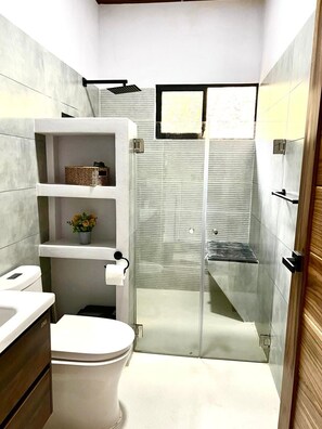 Un baño moderno con inodoro, cabina de ducha de vidrio y lavamanos blanco.
