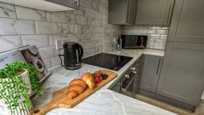 A modern kitchen with a marble backsplash, stainless steel appliances, and a wooden cutting board with croissants and fruit.