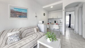 A modern living room with a sofa, a coffee table with a plant, a kitchen area with white cabinets, and a dining area with a chair. - Eva Vacation Home Pool & Relax - Very close to the beach (Puerto del Carmen)