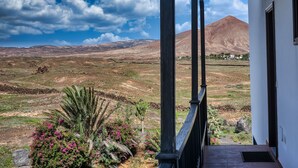 Vista desde un porche cubierto hacia un paisaje montañoso con vegetación escasa y cielo despejado.
