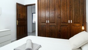 Un dormitorio con un amplio armario de madera, una cama con ropa de cama blanca y una toalla enrollada al lado.