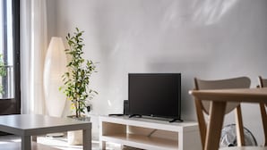 Una sala moderna con un televisor de pantalla plana sobre un soporte blanco, una planta en maceta y una mesa blanca.