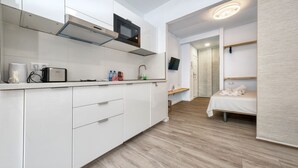 A modern kitchen with white cabinets, a microwave, and a toaster. There is a small dining area with a table and chairs. A bed is visible in the background. - Studio el Greco next to Reducto beach (Arrecife)
