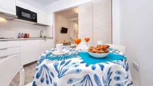 A modern kitchen with white cabinets, a microwave, and a sink. There's a dining area with a table set for two, featuring a blue and white tablecloth, a bowl of croissants, and a glass of orange juice. - Studio el Greco next to Reducto beach (Arrecife)