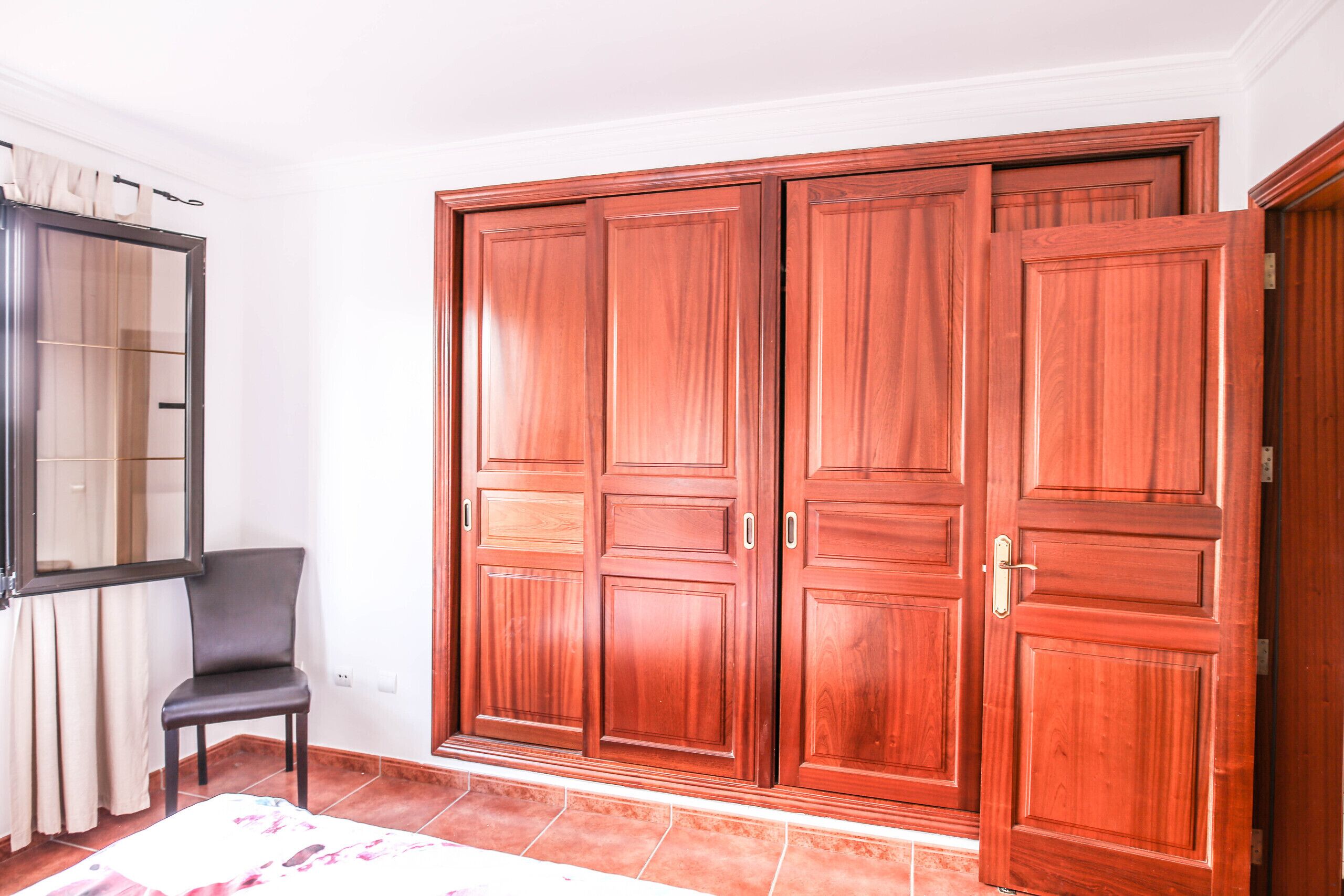 A room with a large wooden wardrobe, a chair, and a radiator.