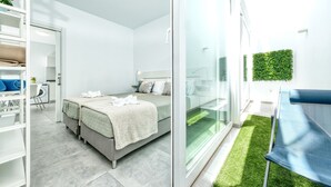 A modern bedroom with a bed, a desk, and a chair. There is a balcony with a view of the sky and a green wall.