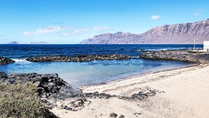 A coastal landscape with clear blue water, rocky shoreline, and a white building.