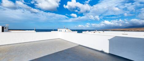 Eine Dachterrasse mit freiem Blick auf das Meer, ein weißes Gebäude und ein Leuchtturm in der Ferne.