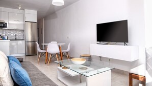Um espaço moderno com cozinha, área de jantar e televisão de tela plana presa a uma parede branca.
