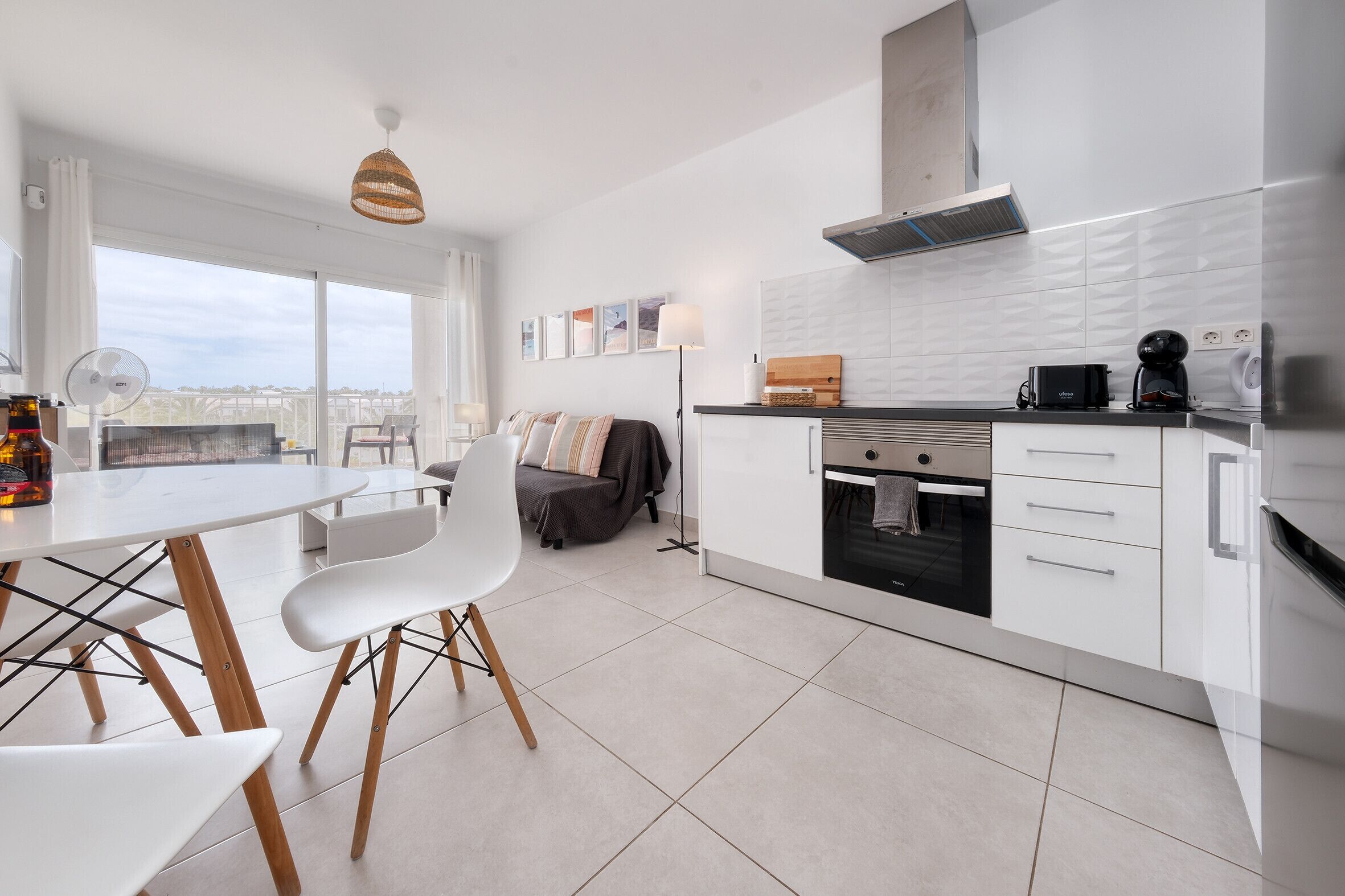 A modern kitchen with white cabinets, a dining area with a white table and chairs, and a large window offering a view.