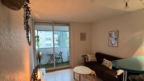Un salon comprenant un canapé, une petite table ronde, une table en verre, un pouf en osier et une plante décorative.
