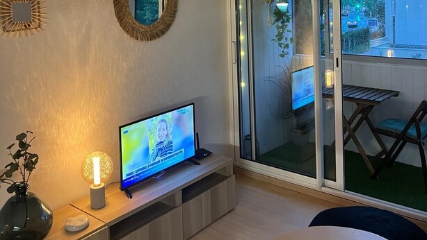 Un salon moderne doté d’un téléviseur à écran plat, d’une porte vitrée donnant sur un balcon et d’un petit coin repas.