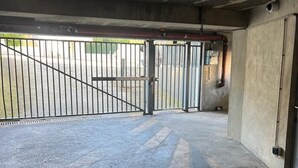 Un espace de stationnement intérieur doté d’un sol en béton, de portails métalliques et d’un mur en béton avec une porte.