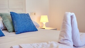 A neatly made bed with blue and green pillows, a white blanket, and a lit bedside lamp.