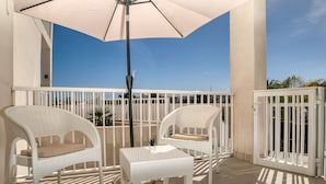 A balcony with two white wicker chairs, a small table, and a large umbrella.