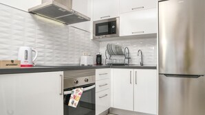 A modern kitchen with white cabinets, a stainless steel refrigerator, a microwave, a toaster, and a kettle.