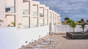 A modern hotel with a row of sun loungers on a wooden deck, a white exterior, and a view of the sea.