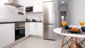 A modern kitchen with stainless steel appliances, a microwave, and a refrigerator. There is a dining table with breakfast items and glasses of orange juice.