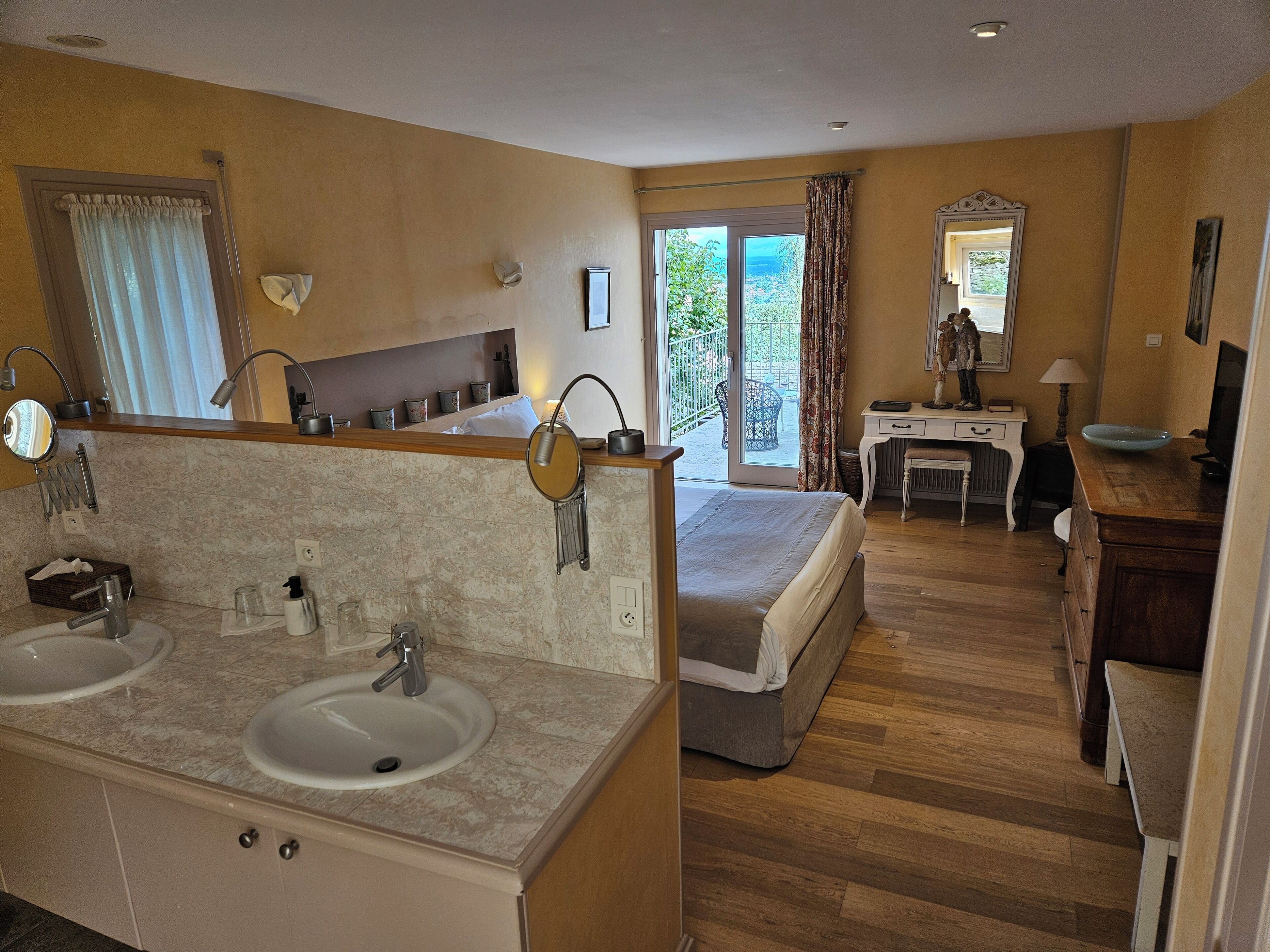 A hotel room with a double sink, a bed, a desk, and a view of the outdoors.