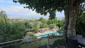 Área de piscina com espreguiçadeiras, um muro de pedra e vista para uma paisagem distante.