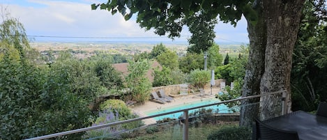 A pool area with lounge chairs, a stone wall, and a view of a distant landscape.